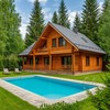 Деревянный коттедж с бассейном на фоне хвойного леса летом