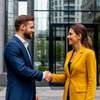Покупатель и продавец пожимают руки на фоне подъезда многоэтажного дома в городе