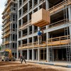 На строительной площадке на одном из этажей новостройки строитель при помощи лебедки поднимает ящик на высоту
