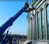 Работа рабочих в люльке автовышки на высоте у фасада здания