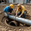 В бетонном коллекторе с трубами идут ремонтные работы - строитель меняет фланец трубы