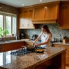 Большая кухня, женщина готовит еду у встроенной в столешницу плиты, на стене плитка из керамогранита