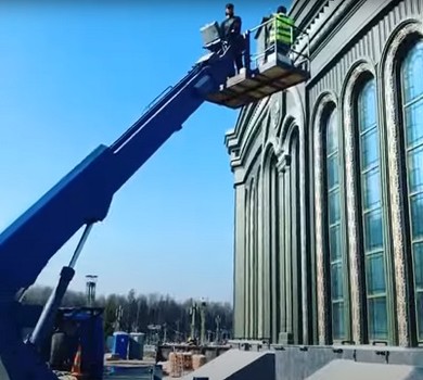 Работа рабочих в люльке автовышки на высоте у фасада здания