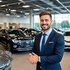 Продавец автомобилей в большом автосалоне радостно встречает новых покупателей